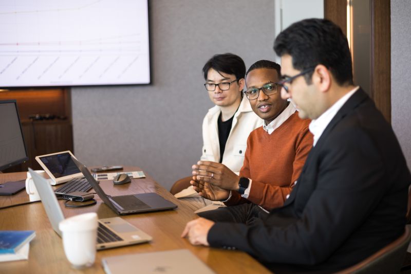 Three men talking at table next to laptops