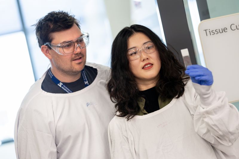 Two researchers in lab coats looking at a pathology slide being held up