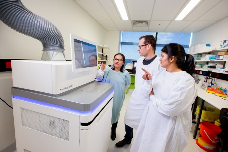Three people standing in front of a large machine in lab coats