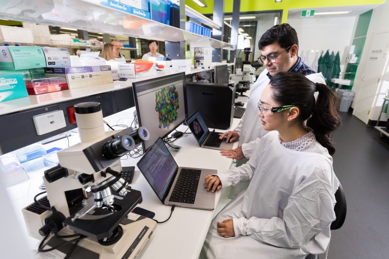Two researchers in lab gear looking at computer screen
