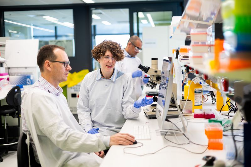Two researchers in lab coats looking at computer screen together