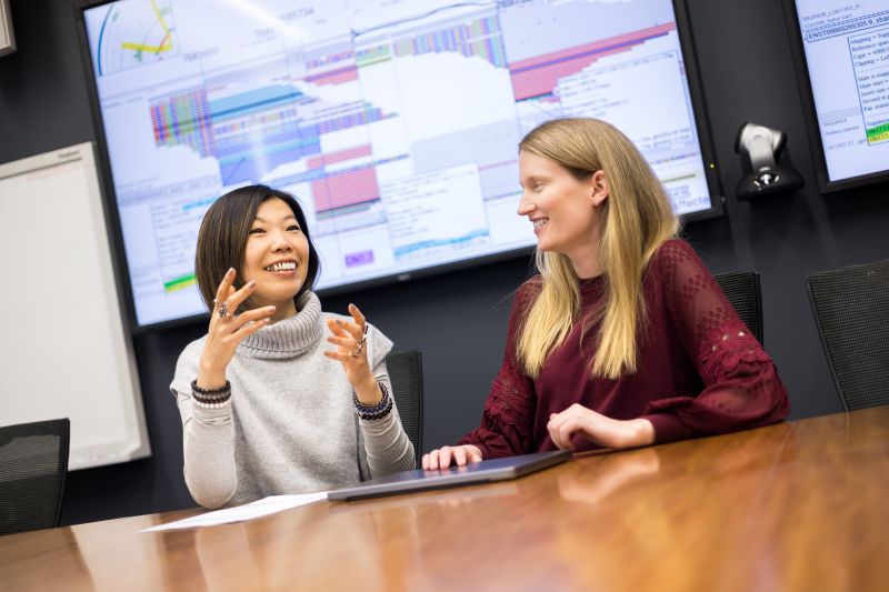 Two women sitting at large desk talking and making hand gestures