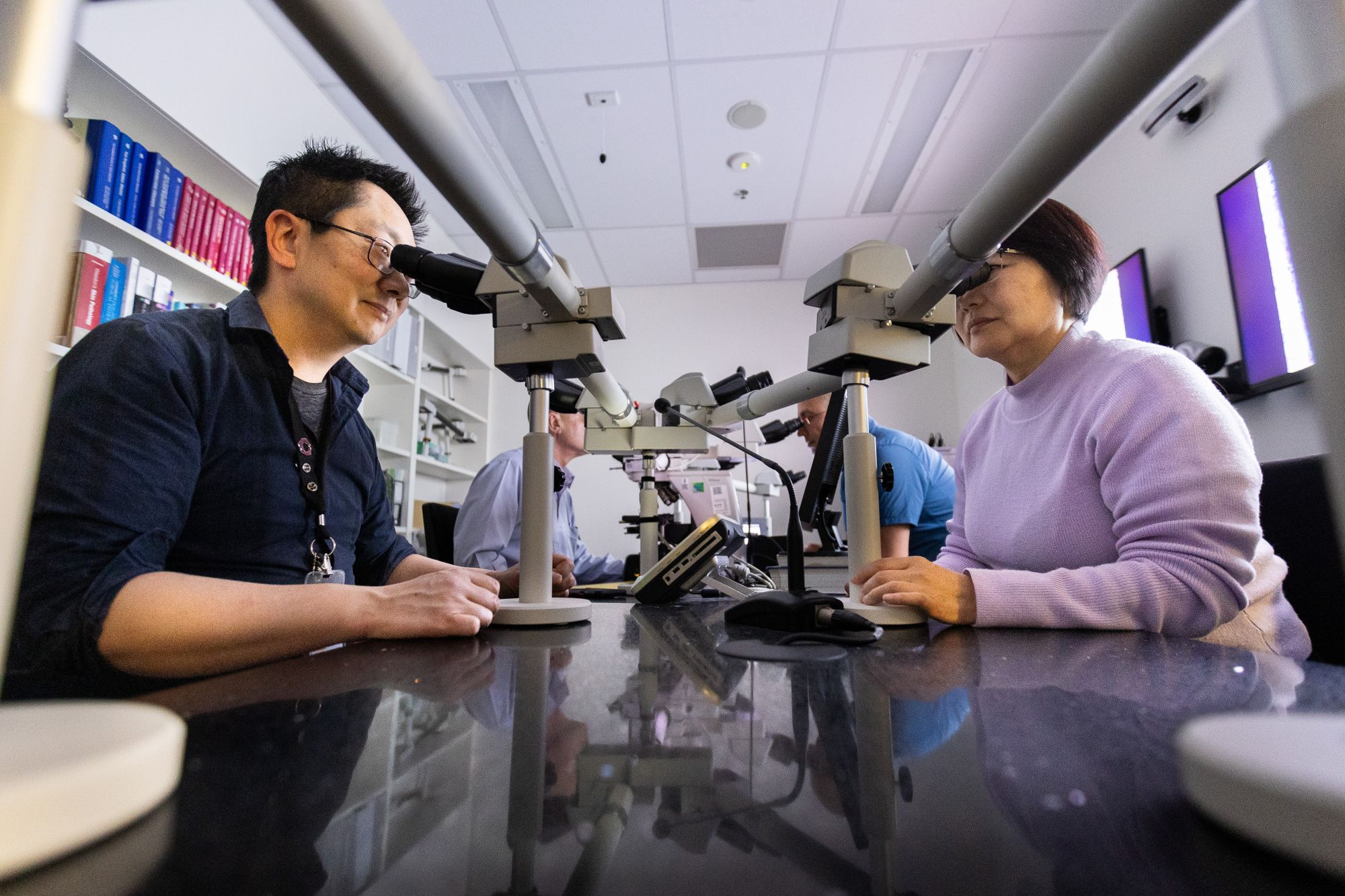 Two people looking into microscope with multiple eye lenses